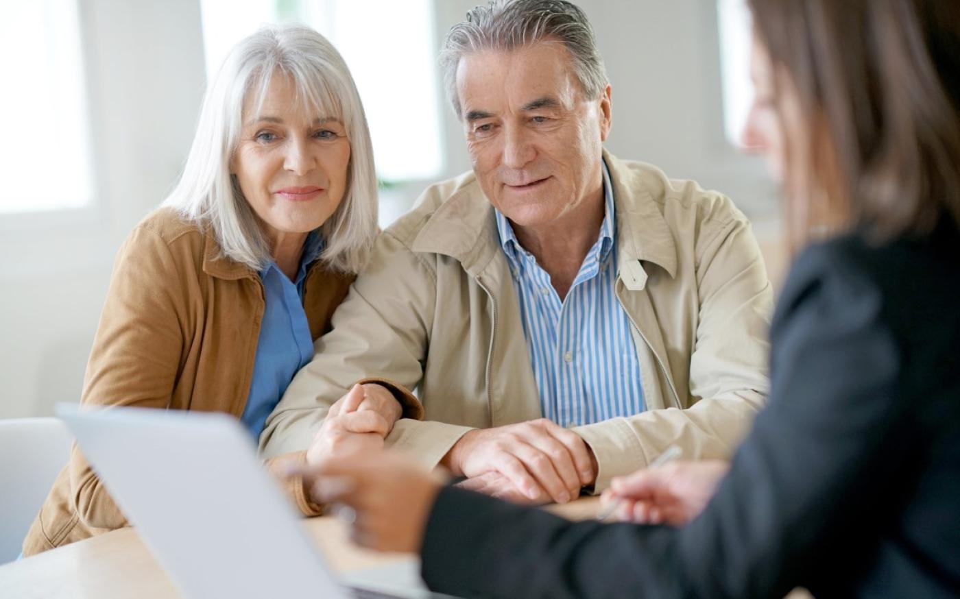 A retiree couple in a meeting with a professional. They are all looking at a laptop screen